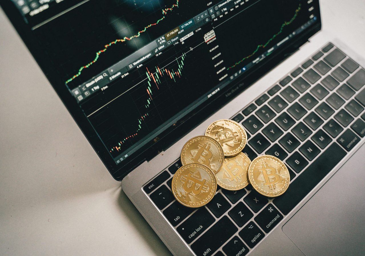 Golden bitcoin coins placed on a laptop keyboard with trading chart displayed on the screen.